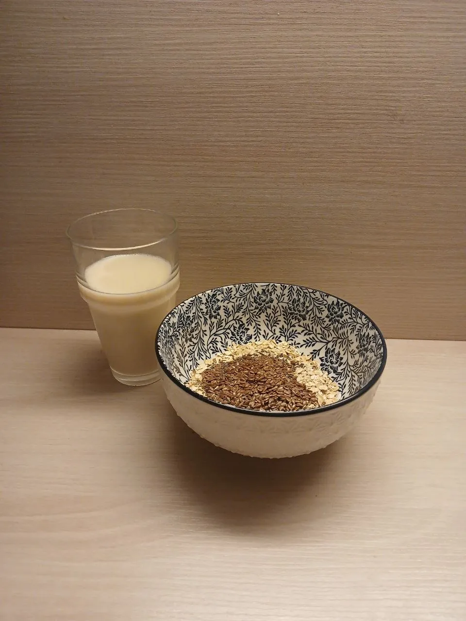 A small breakfast: a light bowl of oats and seeds with a glass of oat milk.